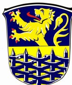 In diesem Bild sehen Sie das Wappen der Gemeinde Flecken Hage. Der Hintergrund ist blau und gelb. Im Vordergrund ist ein blauer Zaun zu sehen. Hinter dem Zaun befindet sich ein gelber Löwe. 
