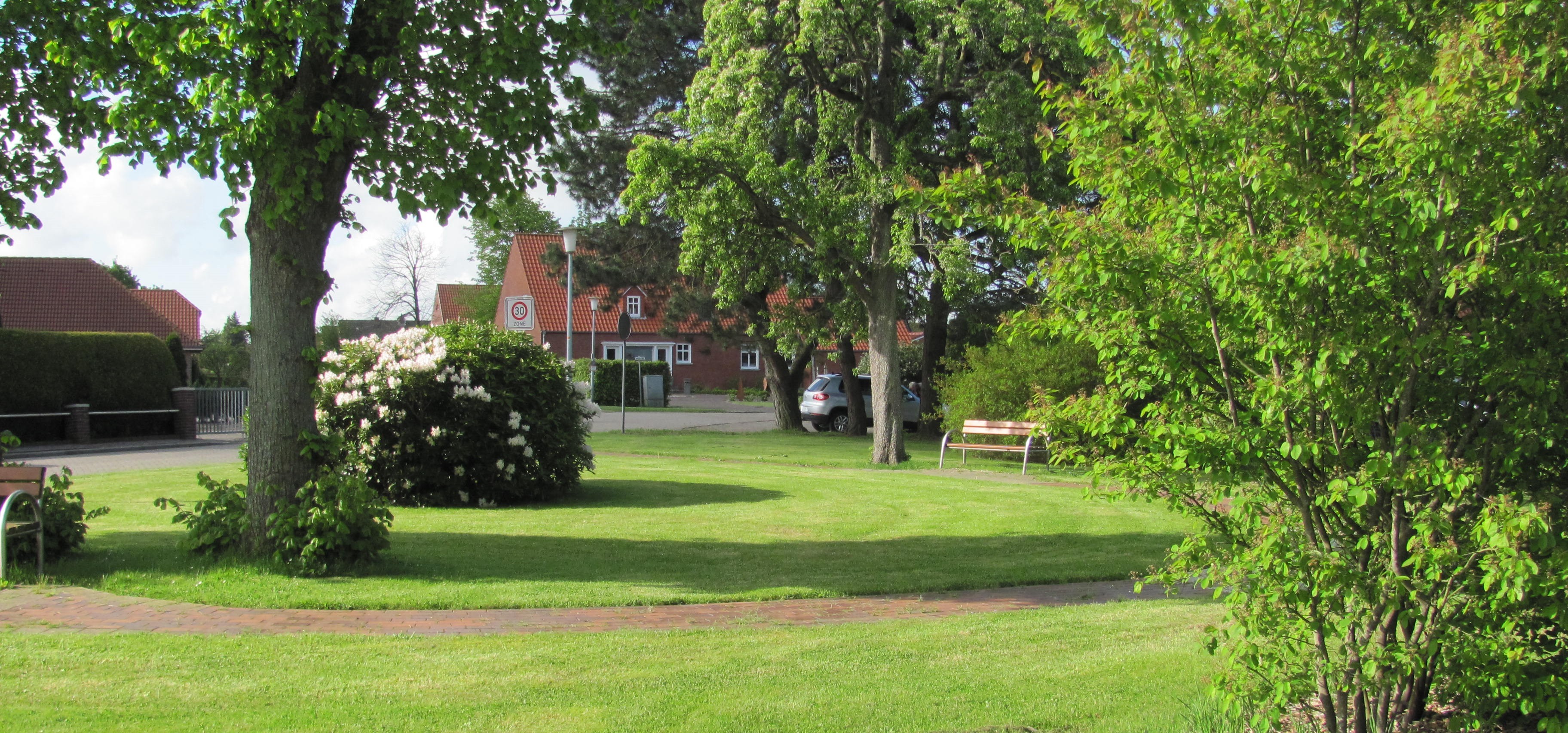 Parkanlage Eckelboomtrift Auf dem Foto ist die Parkanlage an der Ecke Hauptstraße / Eckelboomtrift zu sehen. In Mitten von Pflanzen und Bäumen laden Parkbänke zum gemütlichen Verweilen ein.